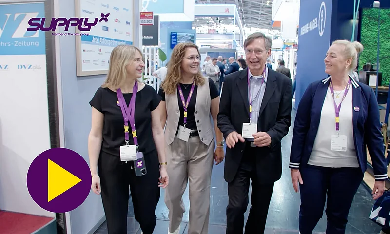 Vier lächelnde SupplyX-Mitarbeiter gehen auf einer Messe oder einem Event-Flur, mit dem SupplyX-Logo im Hintergrund und einem Play-Button, der auf ein Video mit dem Titel "Meet SupplyX – Your logistics partner for Digital Supply Chain Management" hinweist.