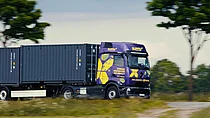 Ein lila SupplyX E-LKW mit Containern fährt auf einer ländlichen Straße.