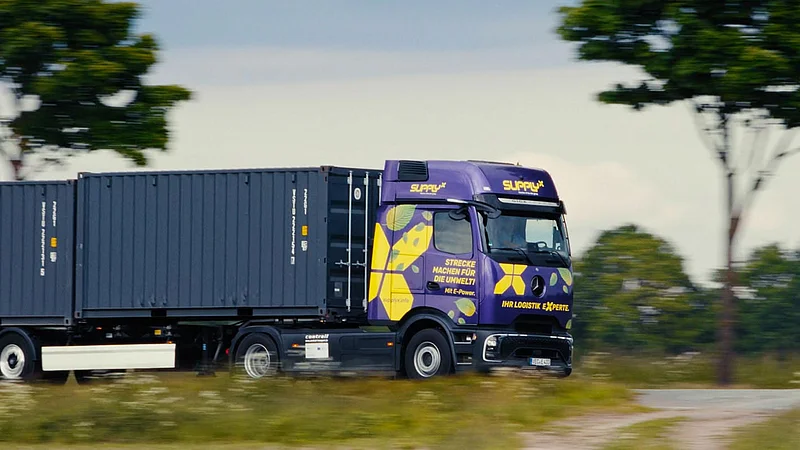 Ein lila SupplyX E-LKW mit Containern fährt auf einer ländlichen Straße.