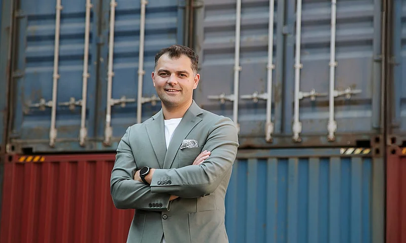 Porträt von Robert Klukowski, dem neuen Leiter der SupplyX-Niederlassung in Gdynia, der lächelt und die Arme verschränkt vor gestapelten Containern steht.