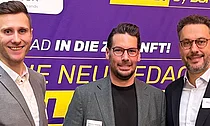 Stephan Pfeifer (Kontakt für AHEAD. By SupplyX), Marco Hoffmeyrer (CEO scoretex) und ein weiterer SupplyX-Vertreter lächeln auf dem BTE-Kongress 2025 vor einem Banner, das Logistik als Gamechanger im Modehandel hervorhebt.