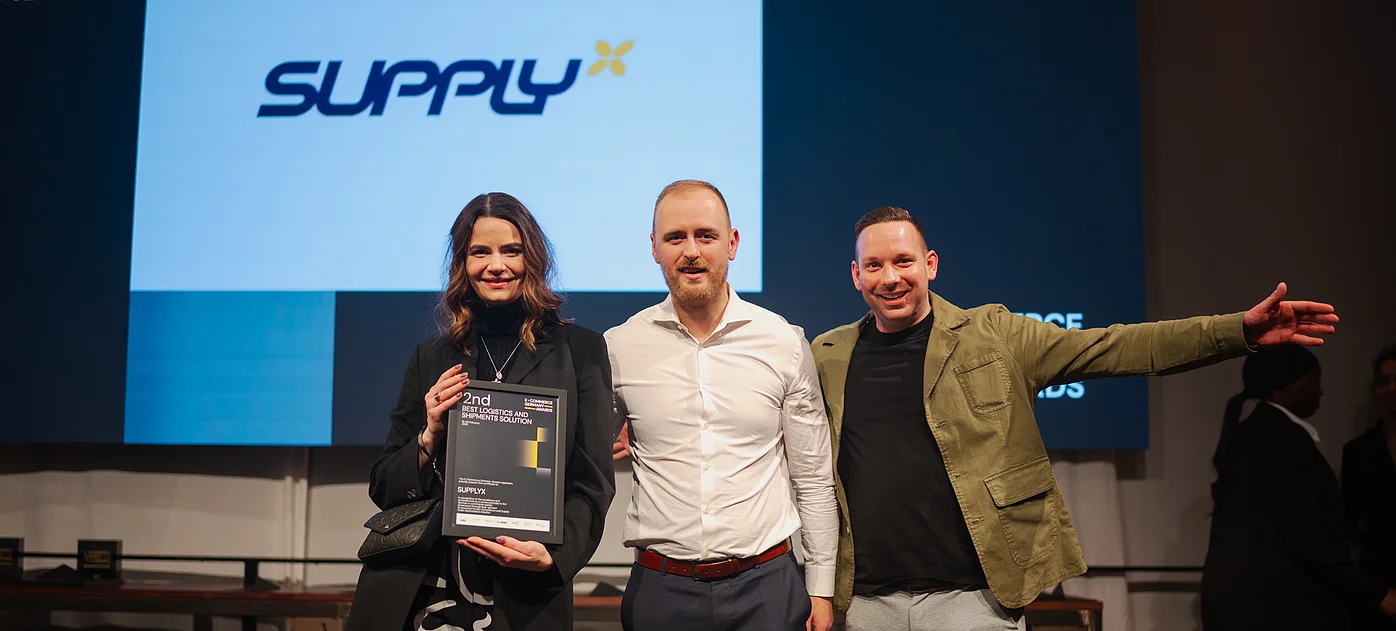 Drei lächelnde SupplyX-Vertreter stehen auf einer Bühne und halten eine Urkunde für den "2nd BEST LOGISTICS AND FULFILLMENT SOLUTION" Award bei den E-Commerce Germany Awards. Das SupplyX-Logo ist im Hintergrund sichtbar.