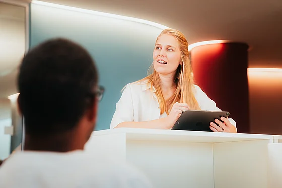 blonde woman stands in the office with man in the foreground
